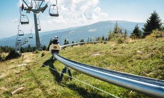 A summer toboggan run in the mountains with chairlifts in the background. The landscape is green and the view of the mountains is beautiful.