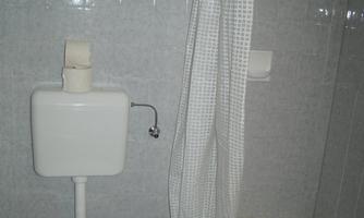 A simple bathroom with a toilet and a shower. The walls are tiled in light colors and the furnishings are functional.