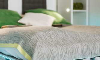 A modern bedroom with a bed made of pallets. The duvet is made of gray fabric, and there are green decorative pillows in the background.