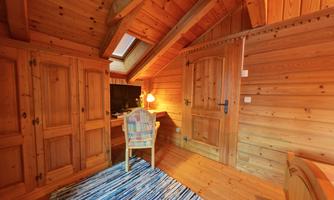 A cozy wooden room with a colorful carpeted area. There is a desk, a chair, and a television.