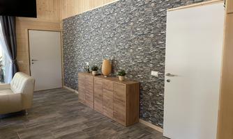 A modern living space with light wood and a stone wall. A wooden cabinet, plants, and a bright door complete the picture.