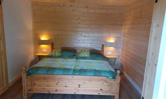 A cozy bedroom with a wooden bed and soft lighting. The walls are made of wood, creating a warm atmosphere.