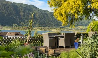 A cozy terrace with garden furniture and a view of the lake and the mountains. The garden is green and blooming, ideal for relaxing outdoors.