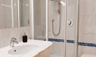 A modern bathroom with a glass shower and an elegant washbasin. The walls are brightly tiled and adorned with blue accents.