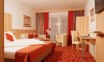 A cozy hotel room with a double bed, a table, and a comfortable armchair. The walls are designed in warm colors with decorative curtains.