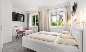 A bright bedroom with a double bed and a television on the wall. Large windows provide plenty of daylight and a friendly atmosphere.