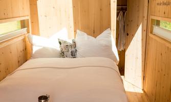 A cozy wooden house with a large bed and plenty of natural light. The decor is simple and inviting, perfect for a relaxing stay.