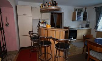 A modern kitchen with a bar and high chairs. In the background, there is a refrigerator and various kitchen cabinets visible.