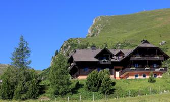 A beautiful wooden house in green countryside. Mountains and trees surround the idyllic setting.