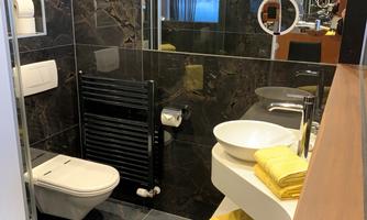 A modern bathroom with black marble elements. Yellow towels and a stylish shower are visible.