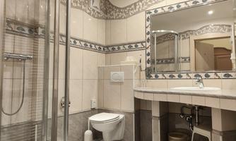 A modern bathroom with a shower cabin, a sink, and a mirror. The walls are designed with bright tiles and a decorative pattern.