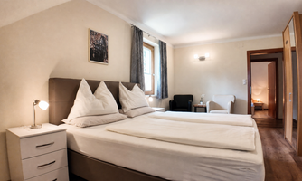 A cozy bedroom with large boxspring beds, each with 2 pillows and bedding. There is also a nightstand and a comfortable seating area.