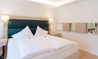 A modern bedroom with a large bed and white bed covers. The walls are light and there are elegant light sources.