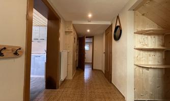 A bright hallway with wooden paneling and a patterned floor. Coat hooks and a round mirror hang on the wall.