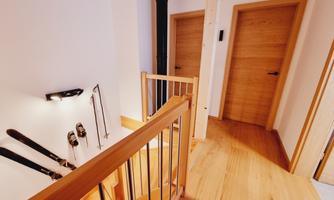 A bright staircase area with a wooden railing and walls. Skis hang on the wall, while the doors are in soft wood tones.
