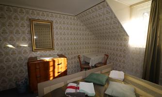 A cozy bedroom with sloped walls and a retro piece of furniture. In daylight, the room shines friendly and inviting.