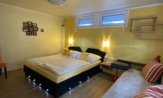 A cozy bedroom with a large double bed and a bright color scheme. There is a seating area with striped cushions and natural light from the windows.