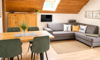 A cozy living area with a dining space and a comfortable sofa. Bright colors and wooden ceilings create an inviting atmosphere.