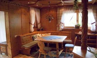 A cozy dining area made of wood with a large corner bench and a table. Windows with curtains let in plenty of daylight.
