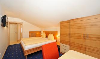 A cozy room with two beds and wooden wardrobes. The room has a television and a simple table.