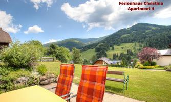 A beautiful view of a green landscape with hills and trees. In the foreground, there are comfortable lounge chairs on a terrace.
