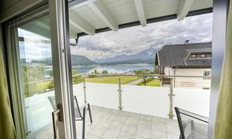 A balcony overlooking a lake and mountains. The view is green and inviting, with a cloudy sky.