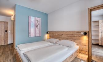 A modern bedroom with wooden details and a comfortable double bed. The walls are painted in calming colors, and there is an accessible bathroom.