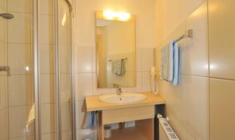 A bright bathroom with a shower and a sink. The walls are tiled, and there is a mirror above the sink.