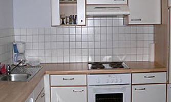 A modern kitchen with white cabinets and a wooden countertop. Equipped with a stove, sink, and a microwave.