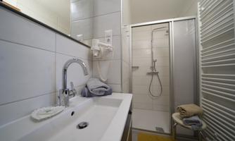 A modern bathroom with a sink and a large shower. The walls are tiled in light colors, and there are towels as well as a chair.