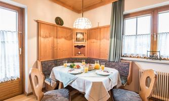 An inviting dining area with wooden furniture and a cozy seating area. The table is set with fresh fruit and drinks.