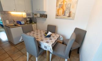A bright kitchen with a dining table and four chairs. A painting with decorative vases hangs on the wall.