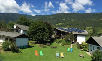 A quiet garden with several houses and reclining chairs. In the background, green mountains and a blue sky can be seen.