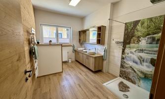 A modern bathroom with wooden paneling and plenty of natural light. The shower features an image of a waterfall, creating a relaxing atmosphere.