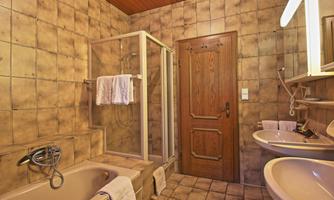 A bathroom with a bathtub, a shower, and two sinks. The walls are decorated with tiles in various earth tones.