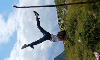 A girl is doing a handstand on a meadow in the mountains. In the background, green hills and a cloudy sky can be seen.