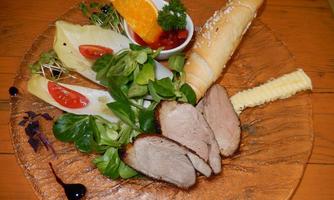 An artfully arranged plate with roasted meat, fresh vegetables, and a delicate sauce. Accompanied by fresh bread and an orange as a garnish.