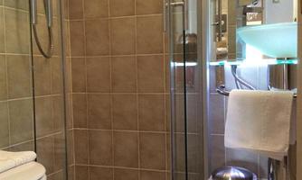 A modern bathroom with a glass shower and elegant tiles. The amenities include towels, toilet paper, and a clear wash area.