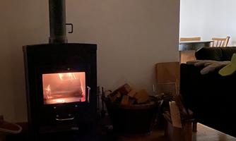 A cozy room with a wood stove that radiates a warm light. On a table, there are candles and glasses that create a relaxed atmosphere.