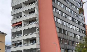 A modern, multi-story residential building with an unusually shaped facade. The colors are neutral with a striking red accent.