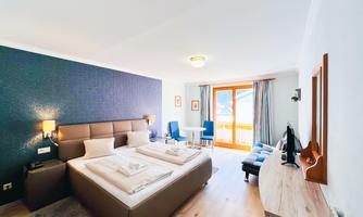 A modern hotel room with two single beds, a table, and chairs. Large windows offer a view outside.