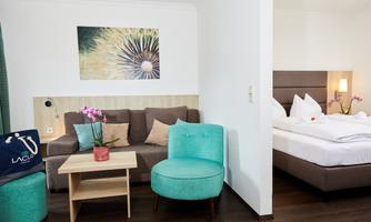 A modern room with a cozy seating area and a beautifully decorated wall. There is a plant on the table, and in the background, a comfortable bed is visible.