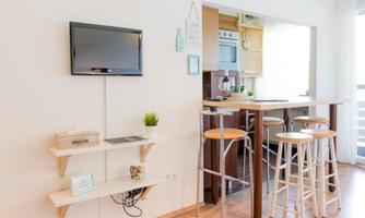 A bright and modern kitchen with bar stools and a flat-screen TV on the wall. The decor is simple and stylish, with an open space concept.