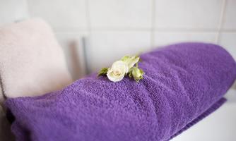 A purple towel lies on a surface, decorated with a white flower. In the background, light gray tiles can be seen.