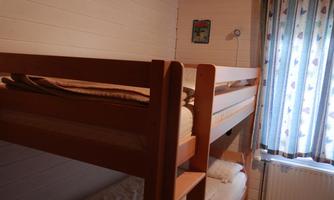 A simple room with a wooden bunk bed. A picture hangs on the wall in front of a window with curtains.