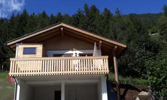 A modern wooden house with a balcony and a beautiful view of the surrounding nature. The facade is bright and inviting, surrounded by trees and green spaces.
