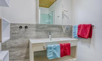 A modern bathroom with a sink and a mirror. Colored towels in red and blue hang on the wall.