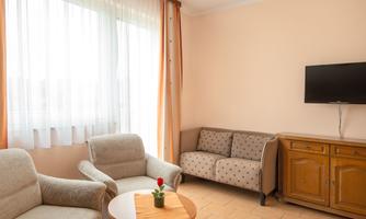 A bright living room with comfortable furniture. A small table with a plant and a television on the wall.