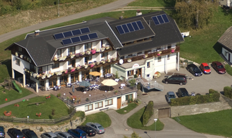 A cozy hotel with a large outdoor seating area and solar panels on the roof. There are plenty of parking spaces and a beautiful landscape surrounding it.