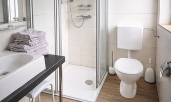 A modern bathroom with a shower, a sink, and a toilet. Towels are neatly stacked on a shelf.